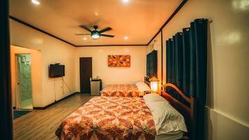 Habitación de hotel con dos camas, ventilador de techo, televisor y una obra de arte colorida en la pared.