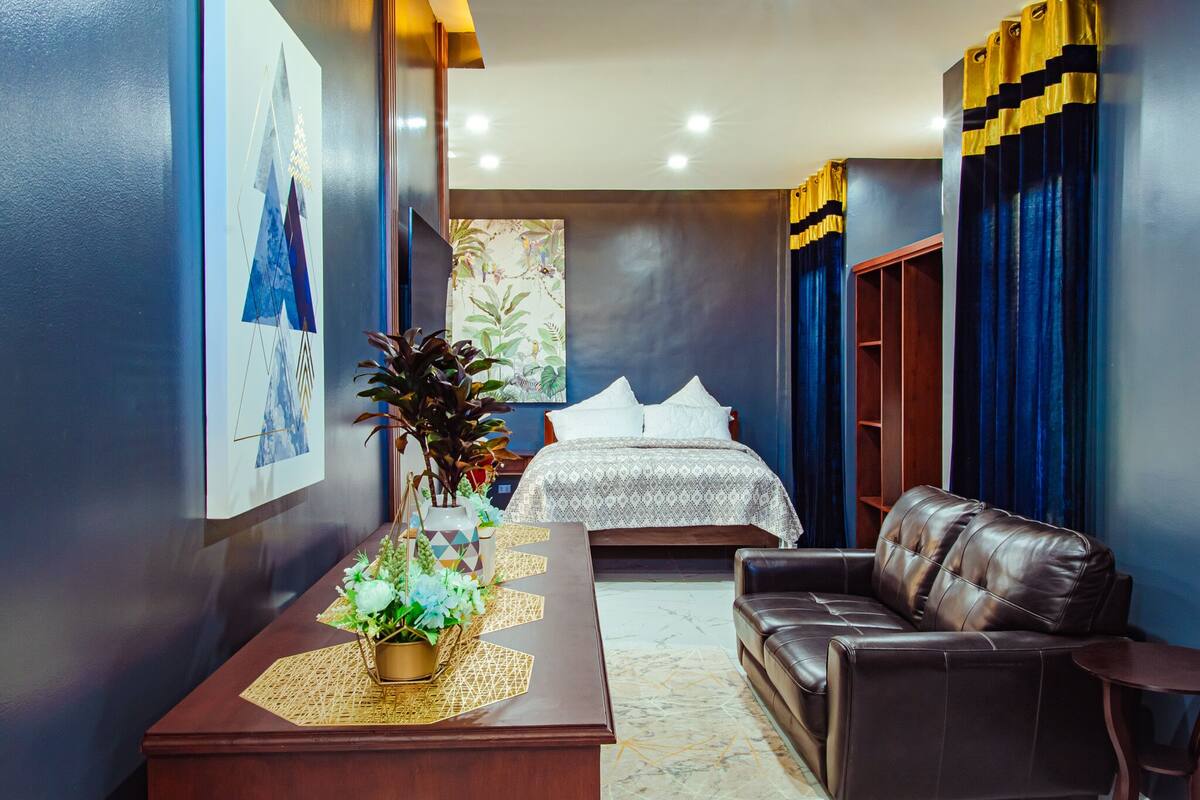 Een hotelkamer met een bed, een leren bank, een nachtkastje van hout en een tv aan de muur.