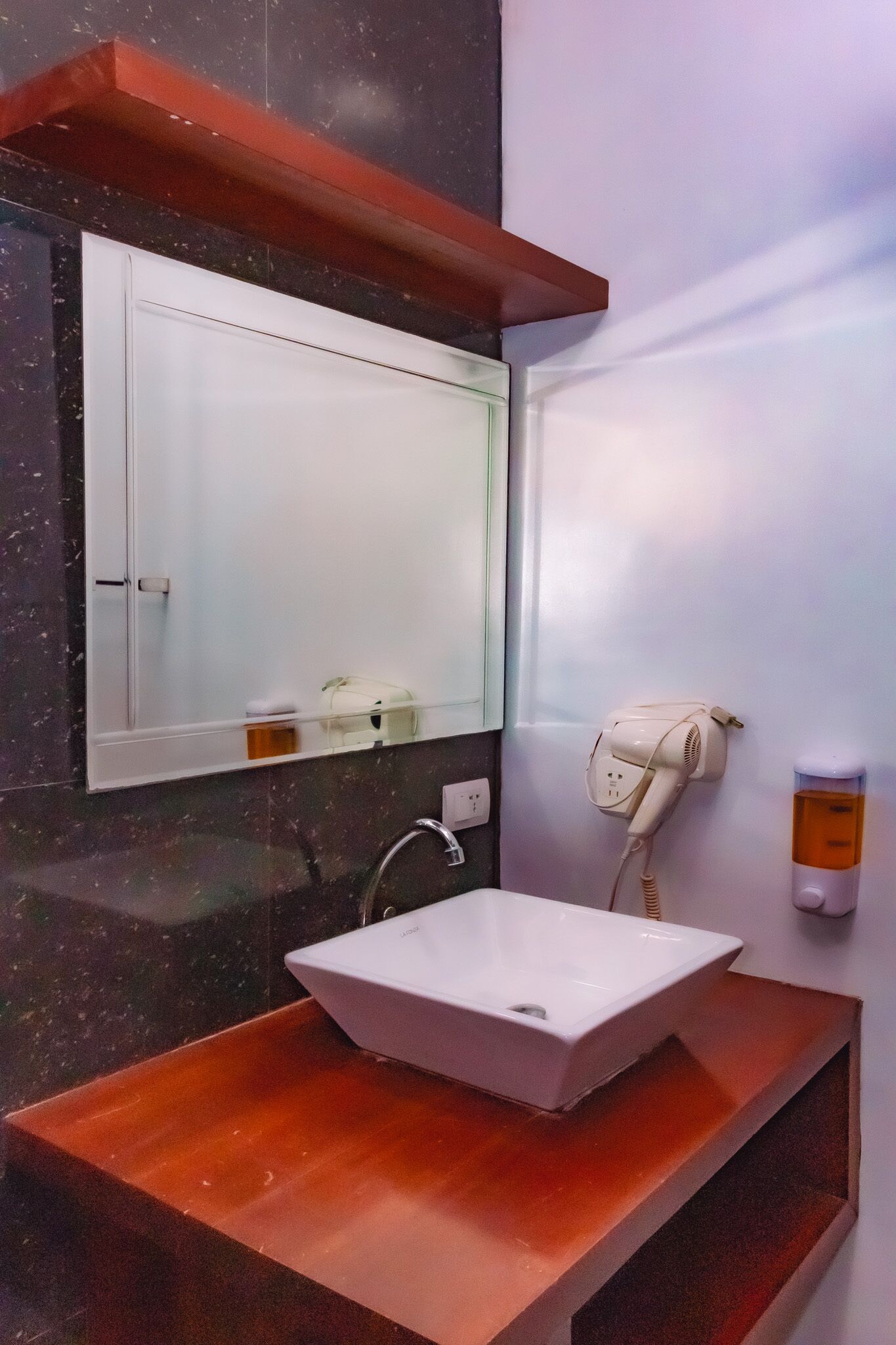 Un baño con lavamanos blanco, espejo, secador de pelo y dispensador de jabón.