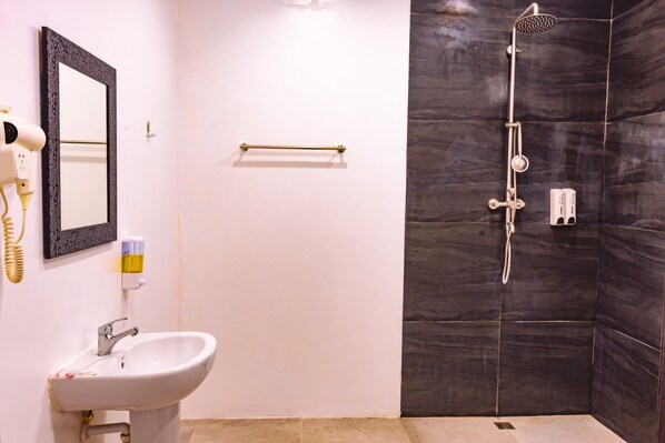 A bathroom with a white sink, a mirror, a hairdryer, a towel rack, and a shower with a handheld showerhead. - Marqis Sunrise Sunset Resort and Spa (Baclayon)