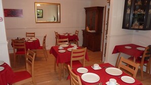 Un comedor con varias mesas dispuestas para cuatro personas, cada una con mantel rojo y platos blancos.