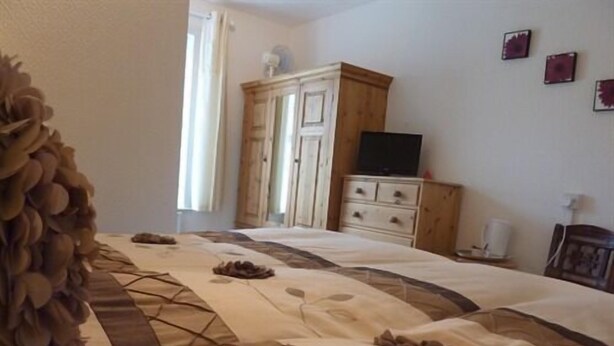 Un dormitorio con una cama, un armario de madera, un televisor y una ventana con cortinas.