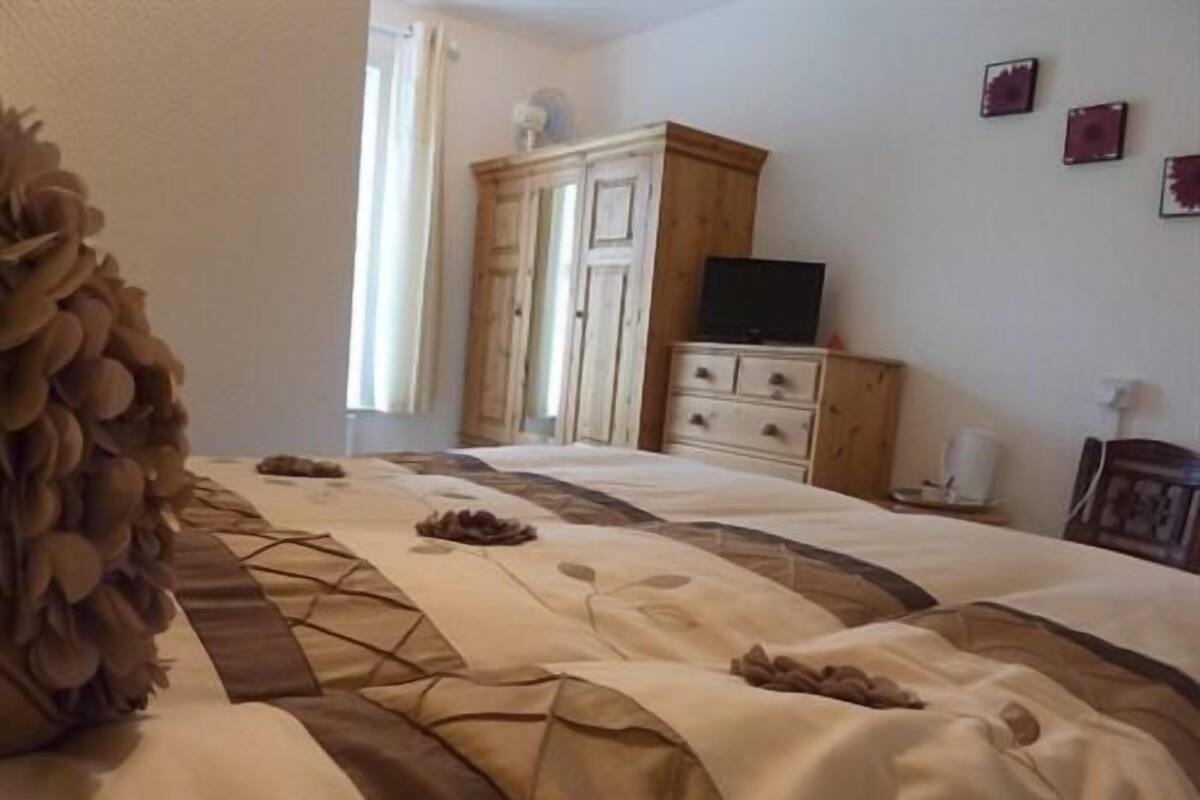 A bedroom with a bed, a wooden wardrobe, a television, and a window with curtains.