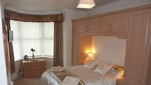 Un dormitorio con cama, armario de madera, lámpara de noche y ventana con cortinas.