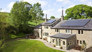 Un edificio de piedra con paneles solares, un patio cubierto de césped y un muro de piedra.