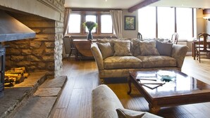 Una sala de estar acogedora con chimenea de piedra, un sofá, una mesa de centro y una zona de comedor con una silla y una mesa.