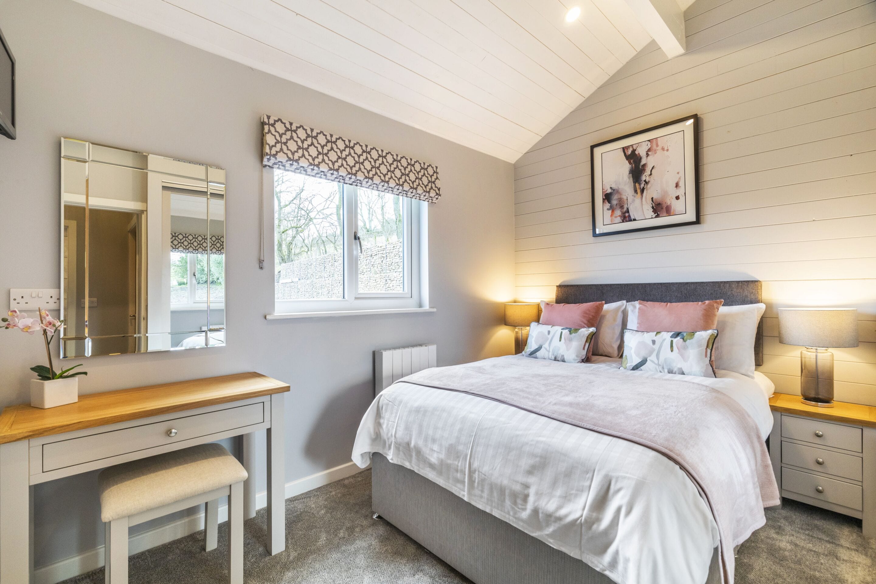 A bedroom with a bed, bedside tables, a desk, a chair, a window, and a mirror.