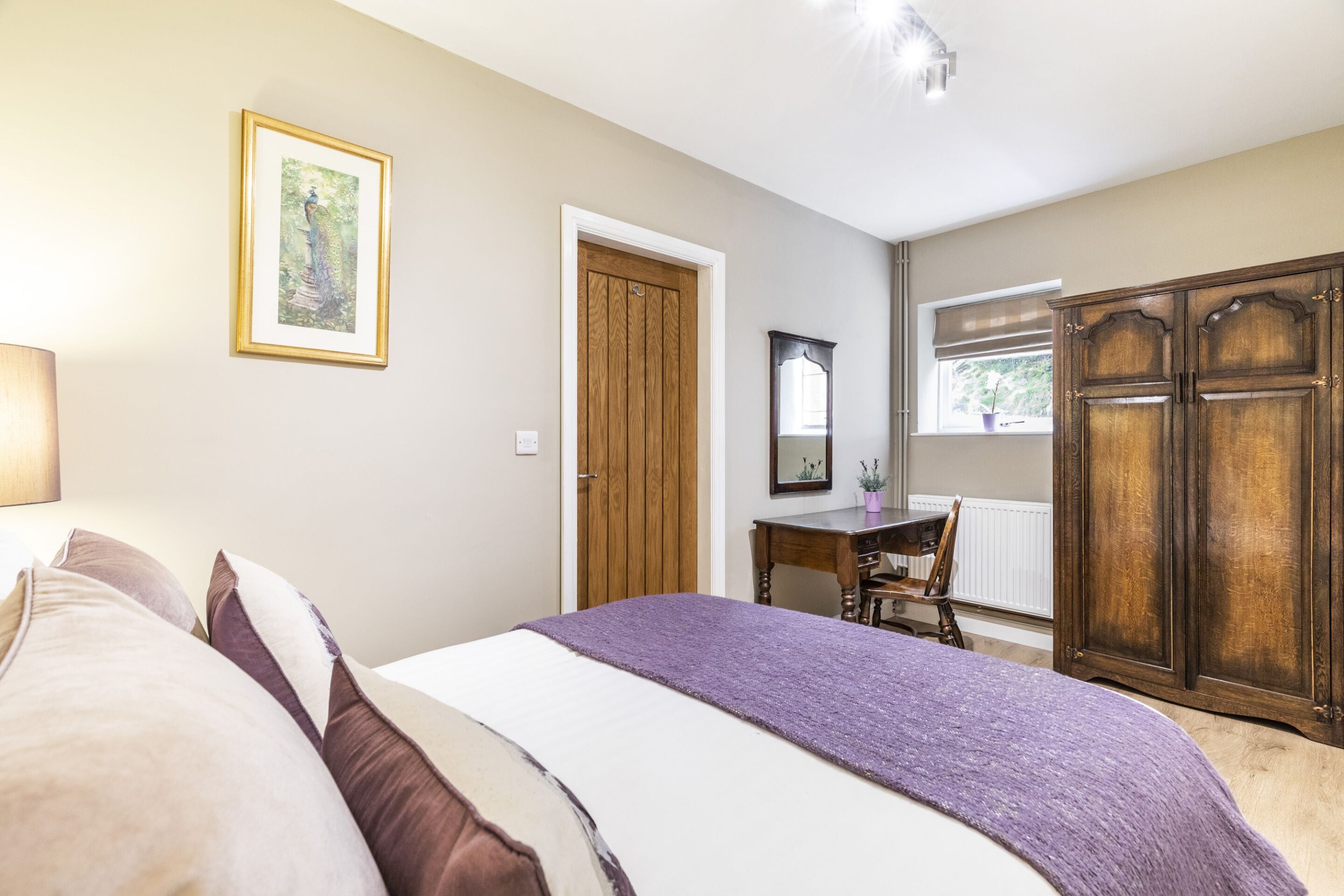 Une chambre à coucher comprenant un lit, un bureau, une chaise, une armoire et une fenêtre donnant sur un paysage verdoyant.