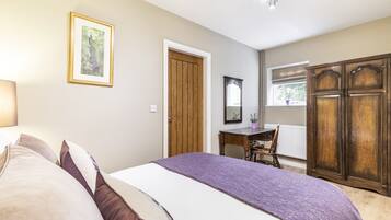 A bedroom with a bed, a desk, a chair, a wardrobe, and a window with a view of greenery.