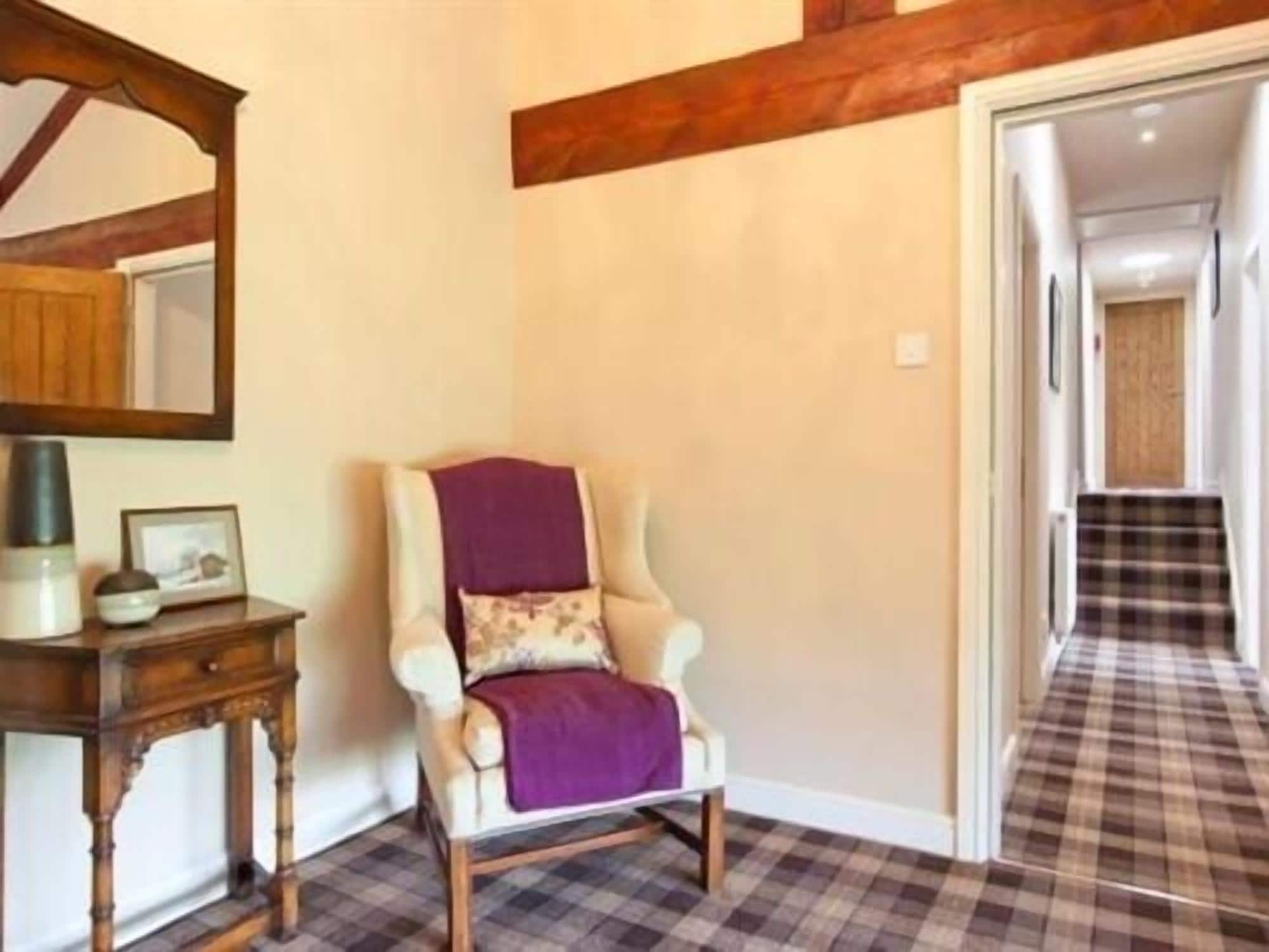 Une chaise recouverte d’un plaid violet, une petite table en bois avec une lampe, et un sol à carreaux.
