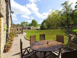 A patio with a round wooden table and chairs, surrounded by potted plants and a stone wall. - Throstle Nest Farm (Skipton)