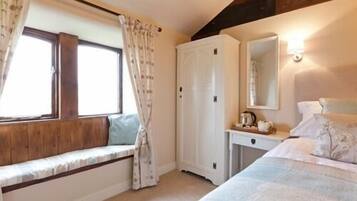 Un dormitorio con cama, mesita de noche, ventana con cortinas, armario y espejo.