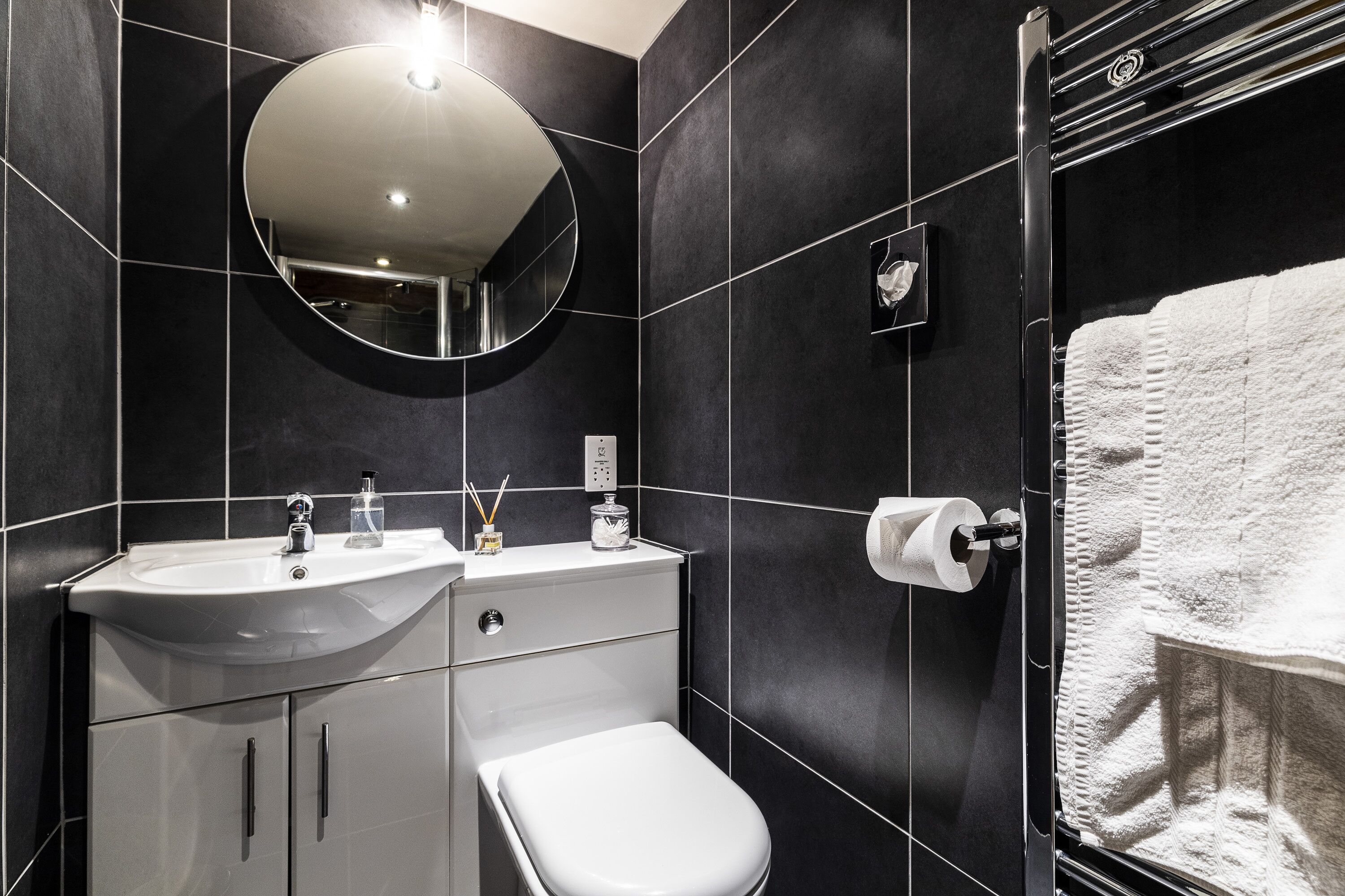 Ein modernes Badezimmer mit Waschbecken, Spiegel und Toilette in Weiß, sowie ein Handtuchhalter mit einem weißen Handtuch.