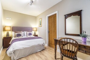A bedroom with a bed, bedside lamps, a wooden door, a desk with a chair, and a mirror. - Throstle Nest Farm (Skipton)