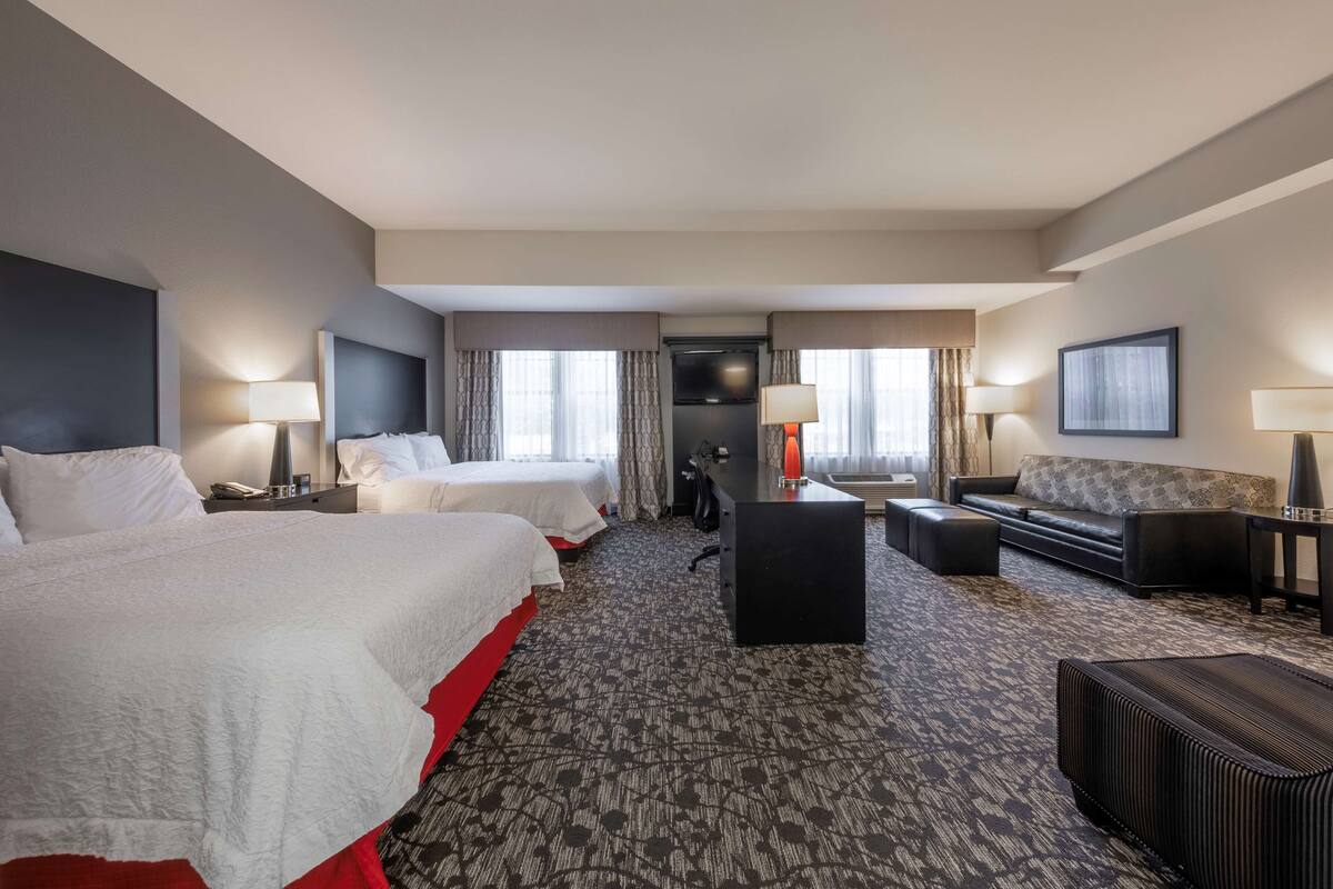 A hotel room with two beds, a sofa, a desk, and a small table.