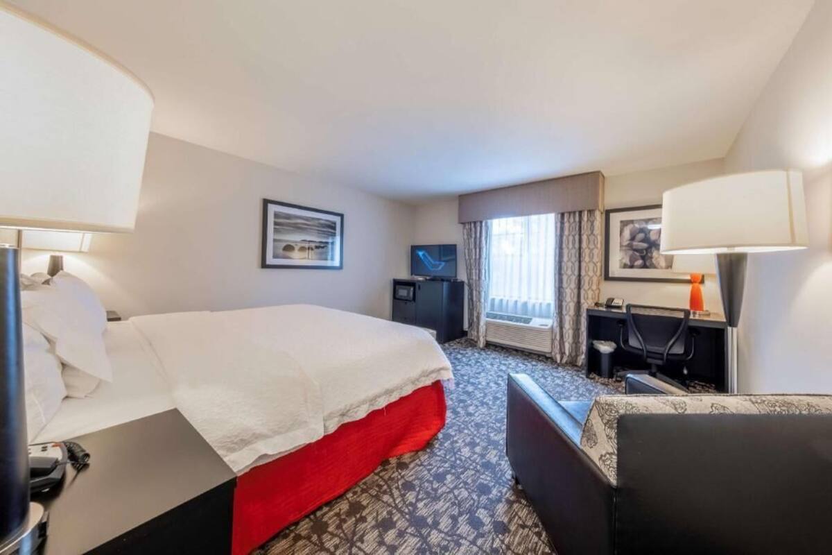 A hotel room with a bed, desk, chair, TV, and window with curtains.