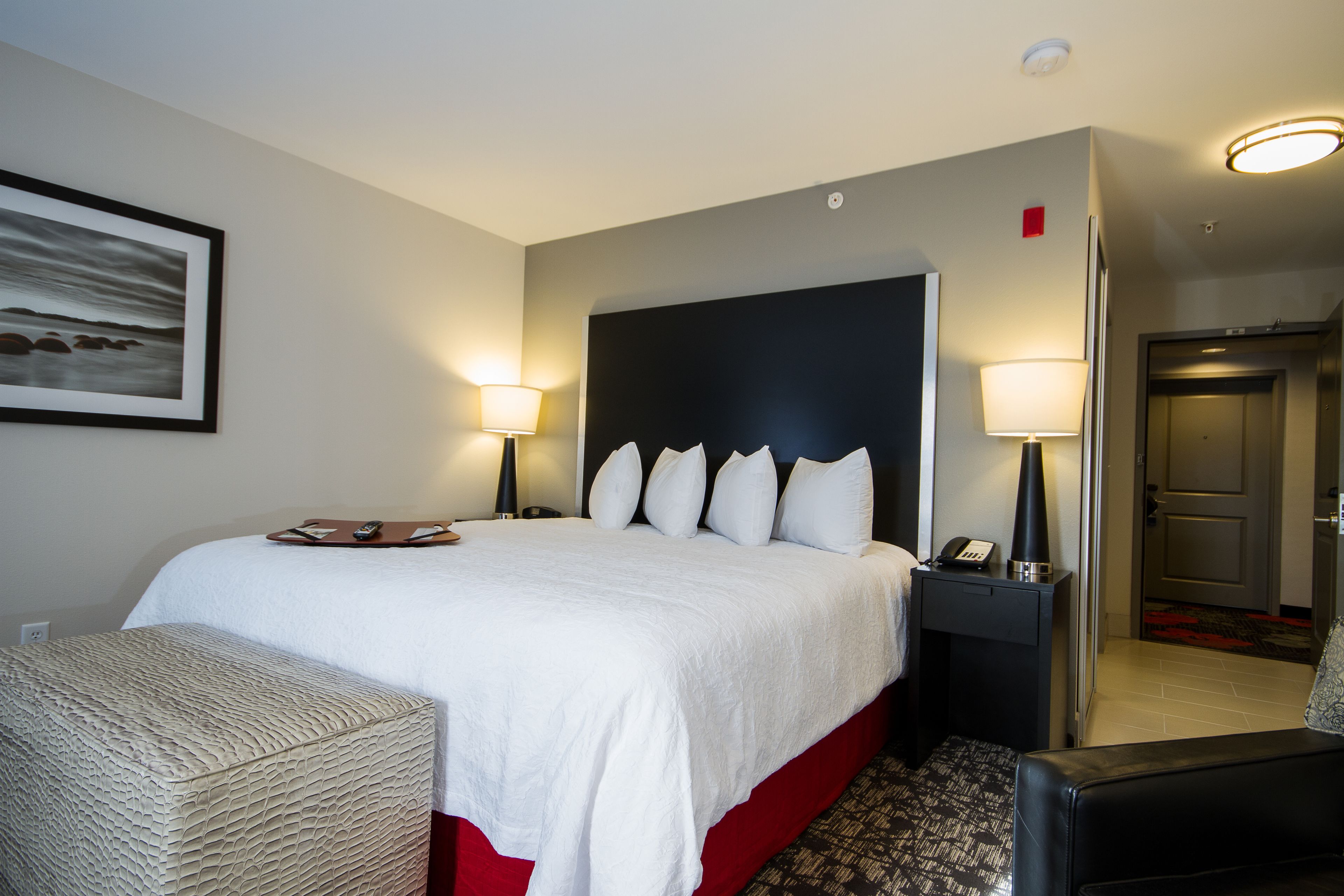 A hotel room with a large bed, two bedside lamps, a nightstand, a chair, and a framed picture on the wall.