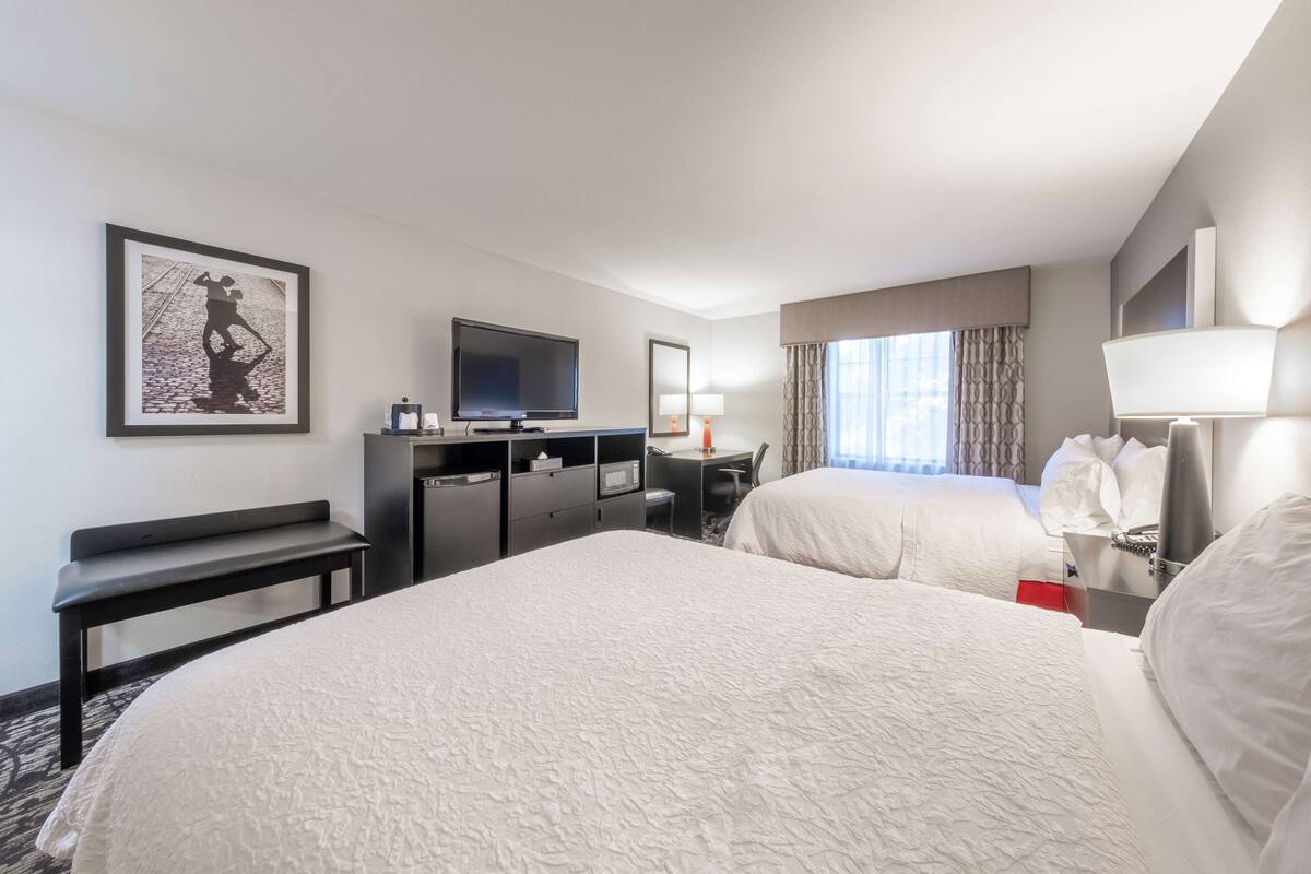 A hotel room with two beds, a desk with a computer, a television, and a framed picture on the wall.