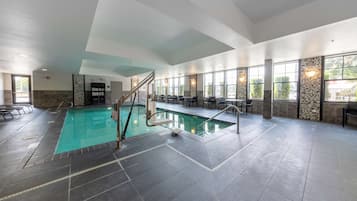Una piscina interior con agua cristalina, rodeada de suelo de baldosas y una zona de estar con sillas y mesas.
