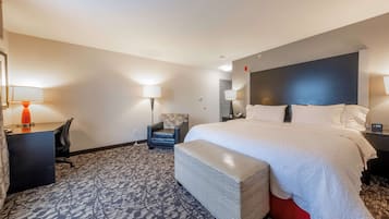 A hotel room with a large bed, a desk with a lamp, a chair, and a patterned carpet.