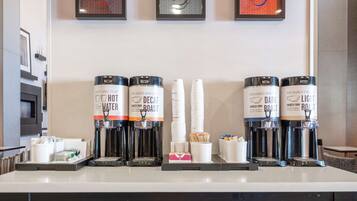 A coffee station with multiple coffee dispensers labeled 'Hot Water' and 'Decaf,' along with disposable cups and a small box of tissues.