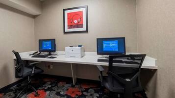 A hotel room with a white desk, two computers, a printer, and two black office chairs.