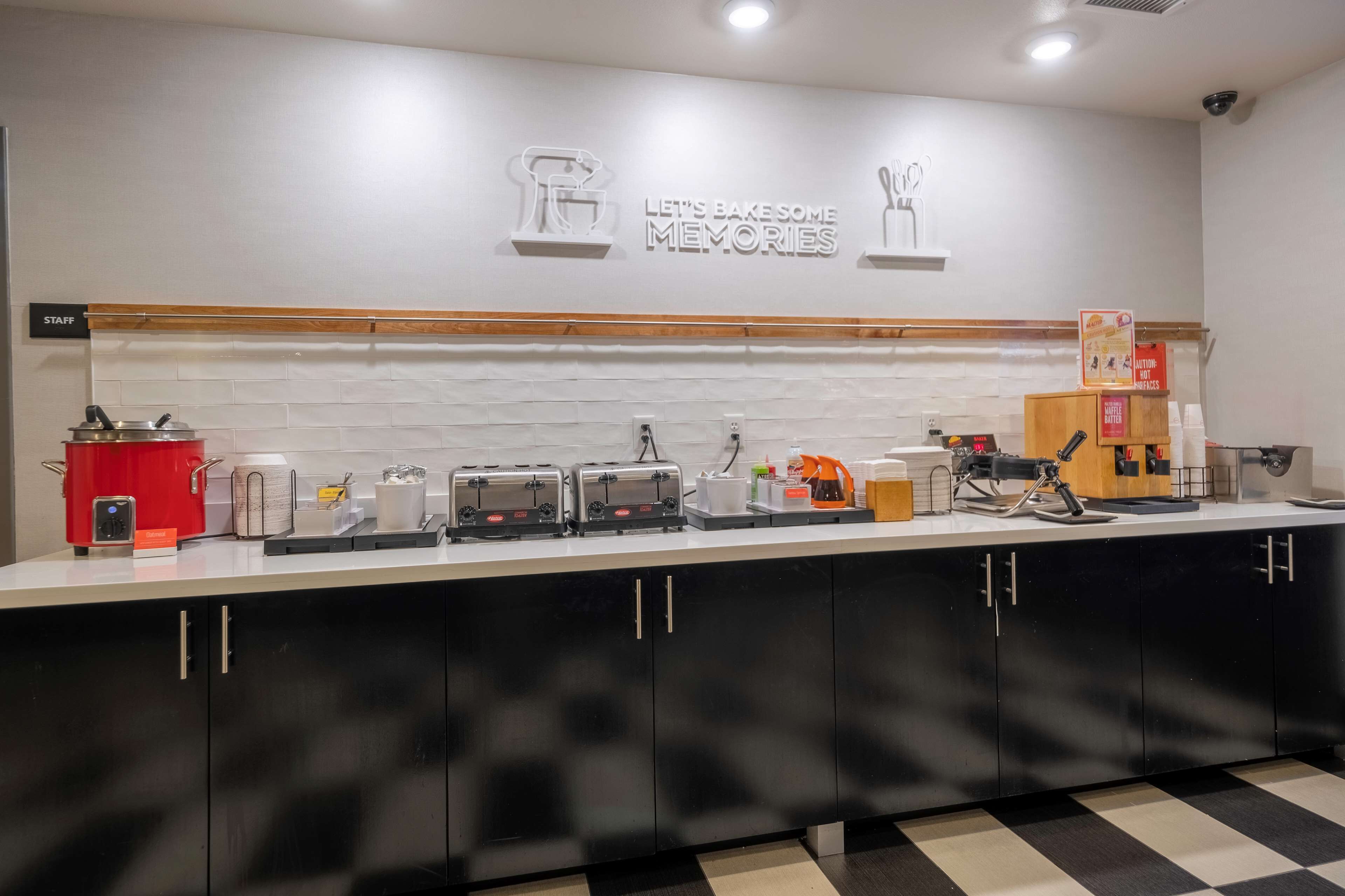 A modern kitchen with a white backsplash, black cabinets, and a 'Let's Bake Some Memories' sign.