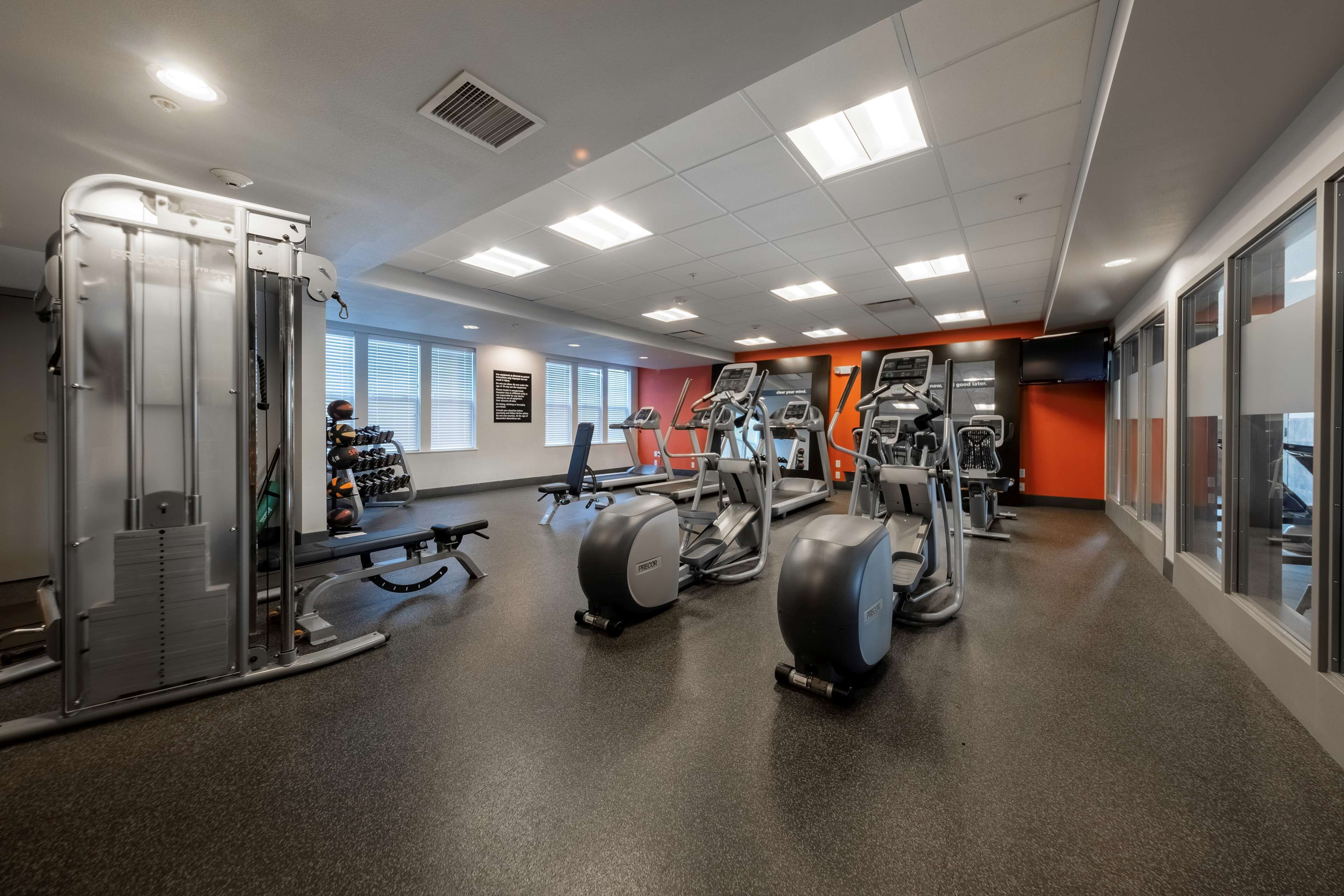 Een sportschool met diverse fitnessapparaten, waaronder loopbanden en krachttrainingsmachines, en een persoon die een roeimachine gebruikt.