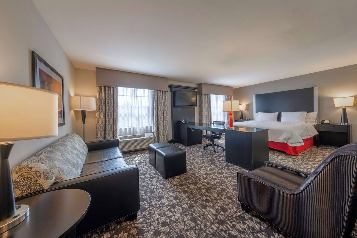 A hotel room with a sofa, a desk, a bed, and a TV.
