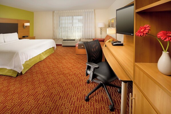 A hotel room with a bed, a desk with a chair, a TV, and a vase with flowers.