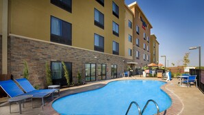 A hotel with a swimming pool, lounge chairs, and a brick wall.