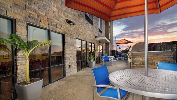 An outdoor patio with a brick wall, potted plants, and a round table with blue chairs.