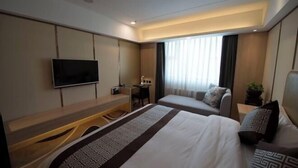 A hotel room with a bed, a desk, a chair, a TV, and a window with curtains.