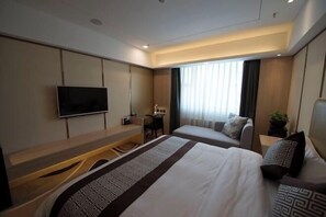 Habitación de hotel con cama, escritorio, silla, televisor y ventana con cortinas.