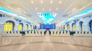 A spacious conference room with a stage, rows of chairs, and large windows with blue curtains.