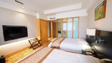 A hotel room with two beds, a TV, a desk, and a window with a view.
