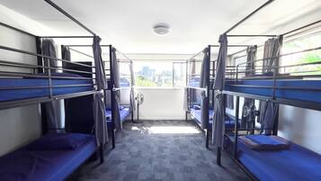 A room with bunk beds, a fan, and a view of buildings through a window.