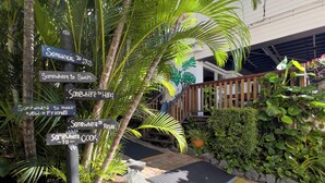 A tropical outdoor area with a signpost listing activities like swimming, relaxing, and cooking. - Somewhere To Stay Backpackers (Highgate Hill)