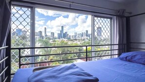 A hotel room with a bed, a window with a view of a city skyline, and a balcony railing. - Somewhere To Stay Backpackers (Highgate Hill)