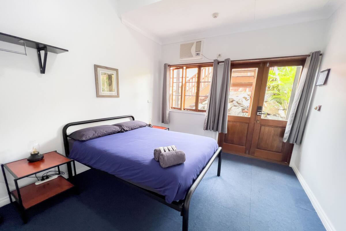 A bedroom with a bed, a nightstand, a window with curtains, and a door leading outside.