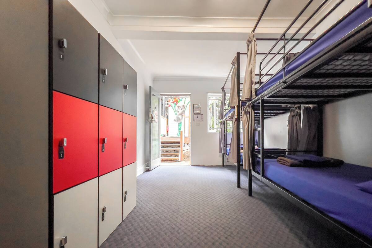 A corridor with bunk beds, lockers, and a door leading to a room with a window.