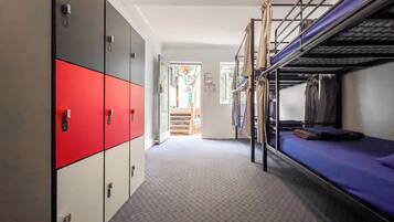 A corridor with bunk beds, lockers, and a door leading to a room with a window.