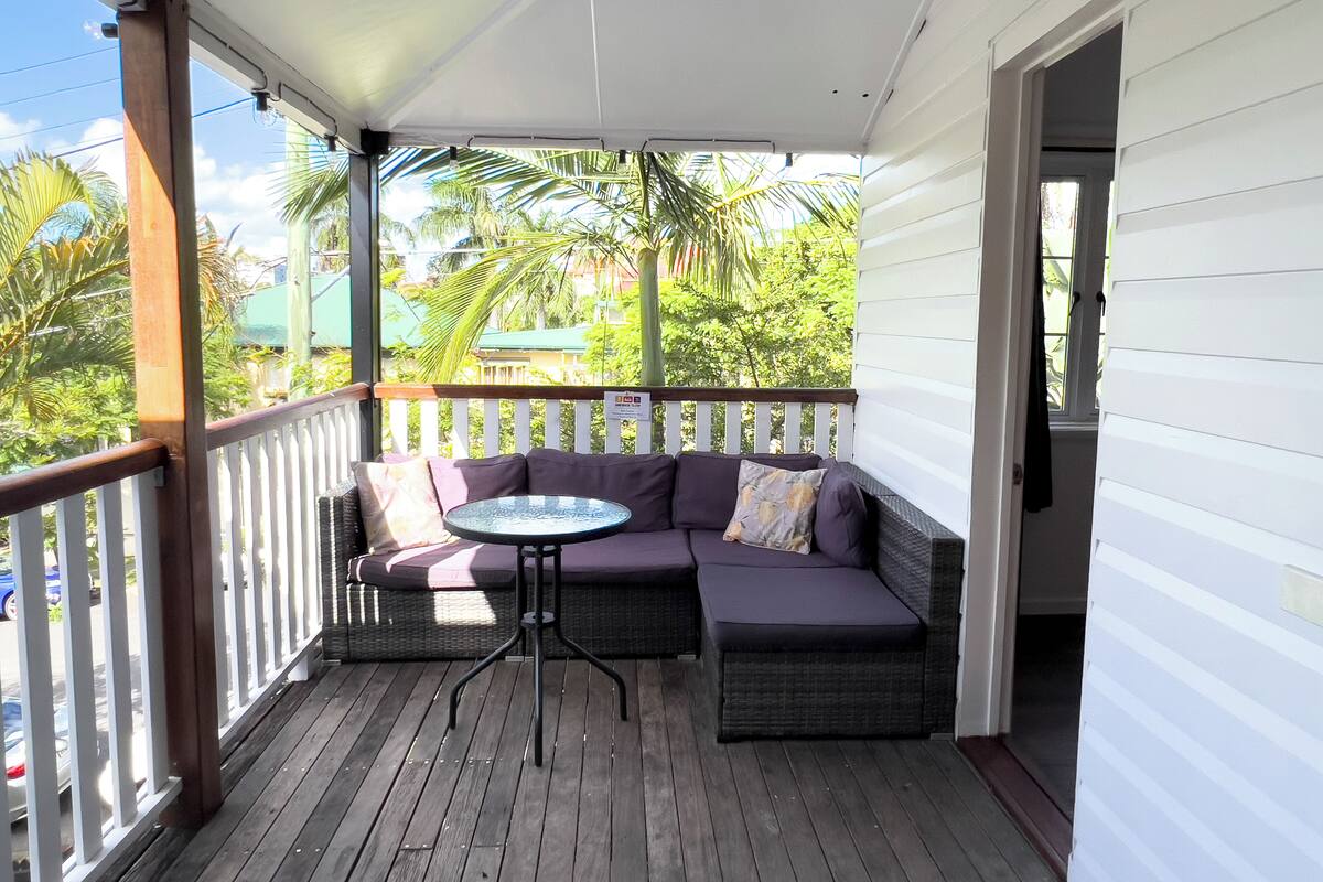 A covered porch with a cushioned seating area and a small table.