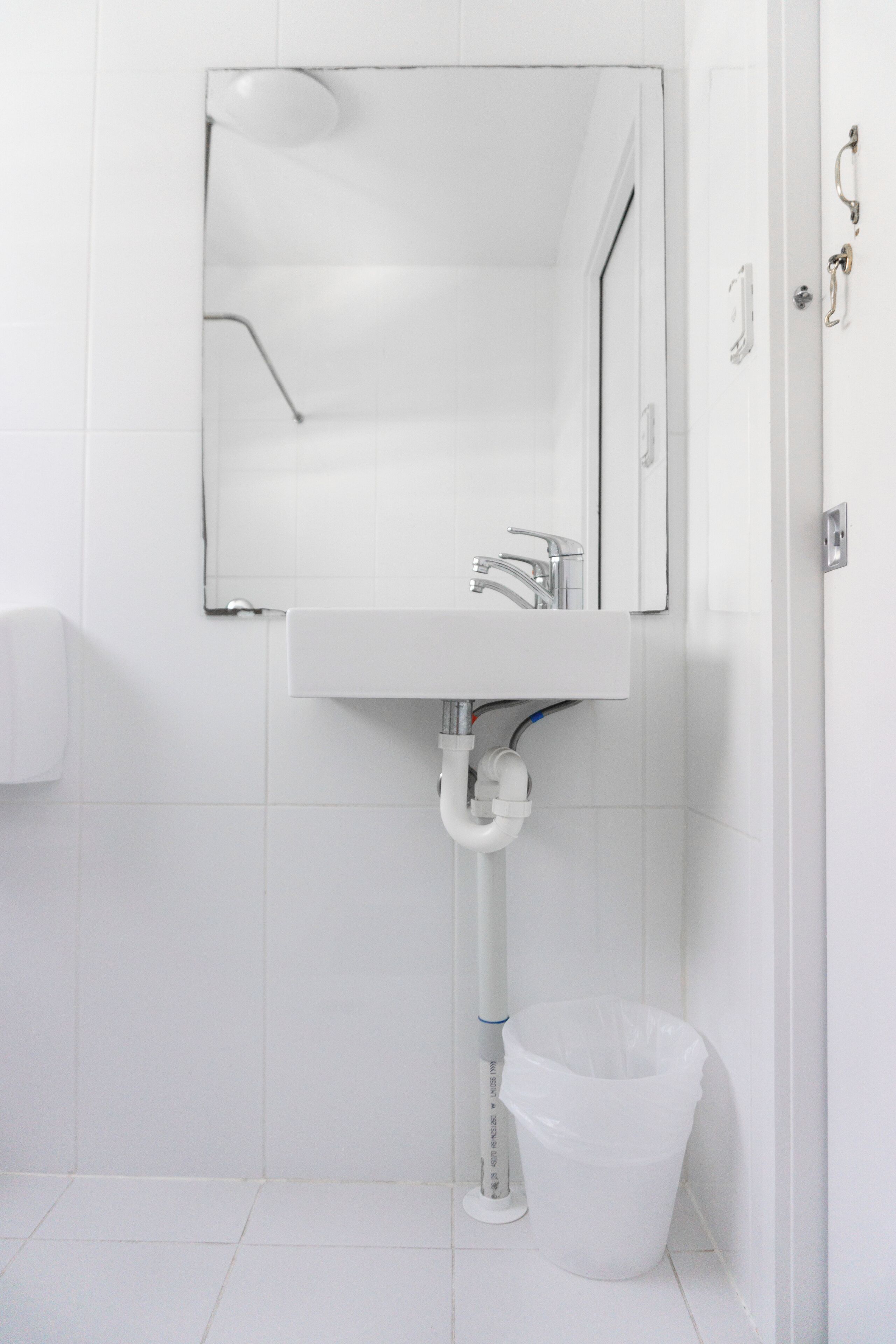 A white bathroom with a sink, mirror, and a trash bin.