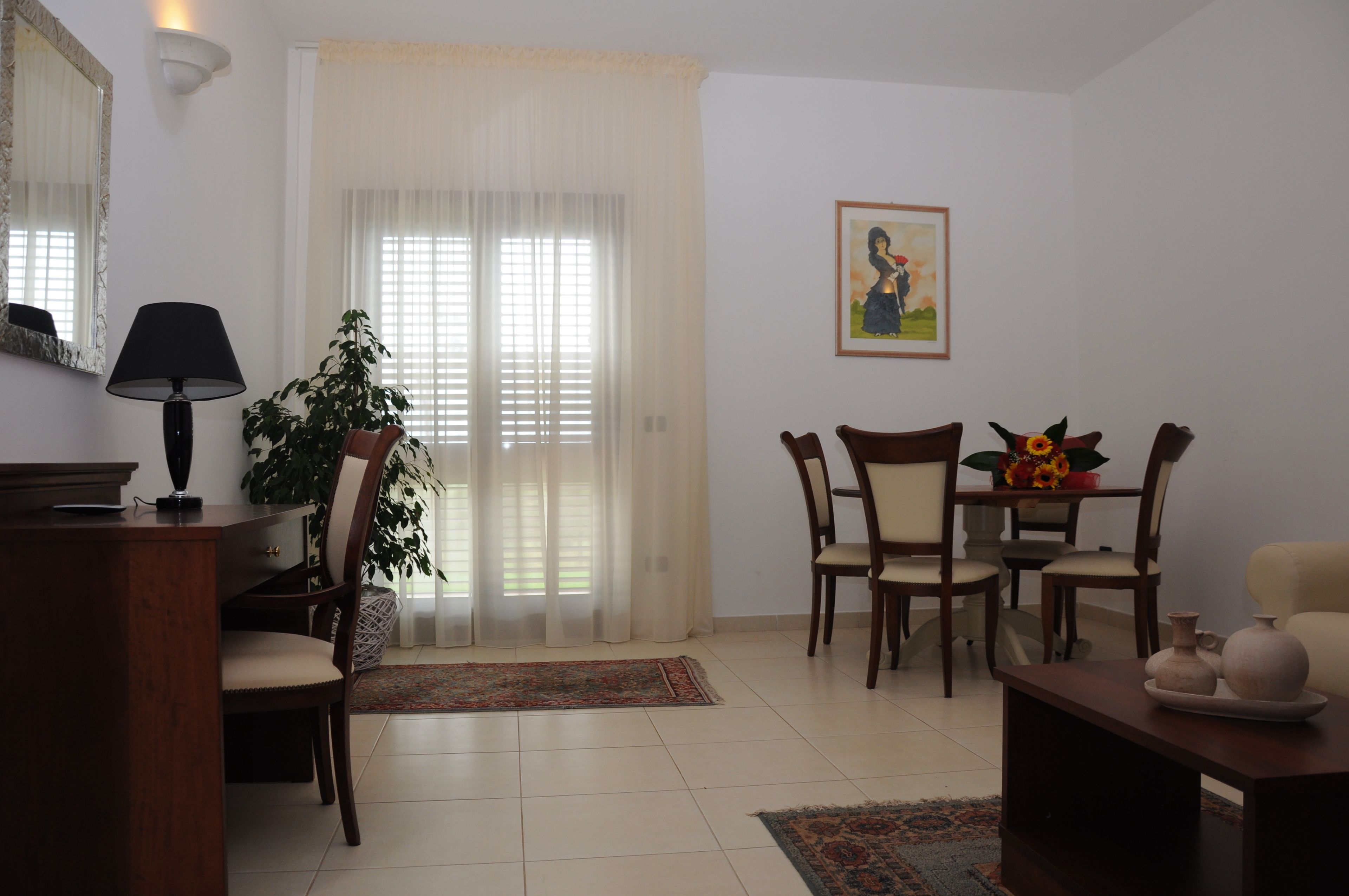 A living room with a dining area, a large plant, a painting, and a lamp.