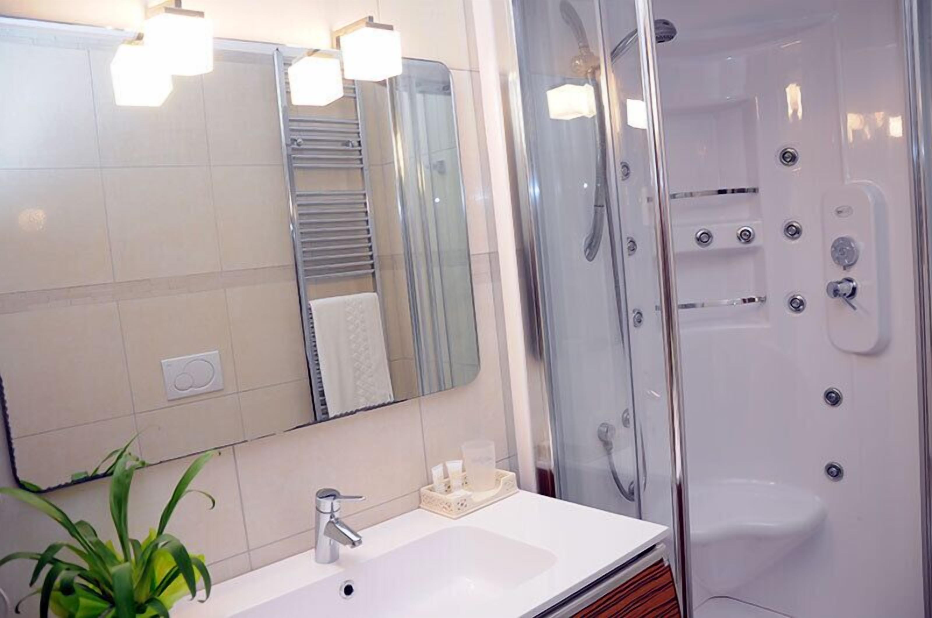 A modern bathroom with a large mirror, a white sink, and a glass-enclosed shower with multiple controls.