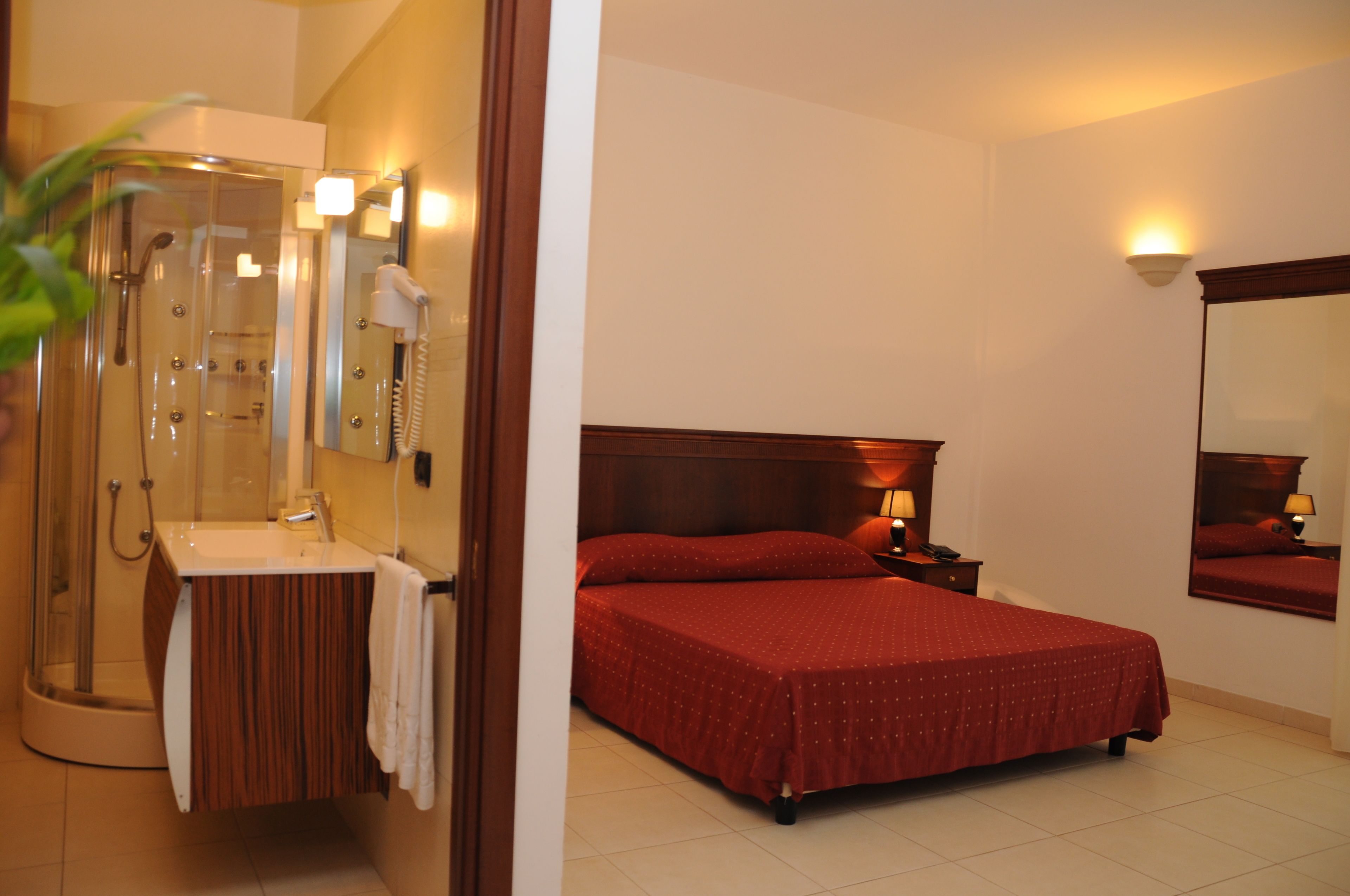 Habitación de hotel con ducha, lavamanos, cama y mesita de noche con lámpara.