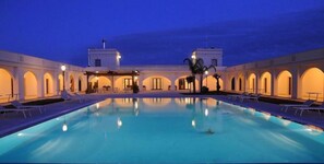 A pool area with lounge chairs and a covered seating area.