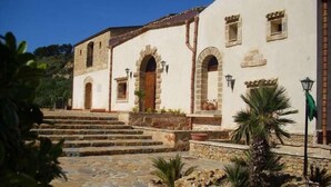 A building with a stone staircase leading to a wooden door, surrounded by stone walls and potted plants. - Casale del Golfo (Alcamo)