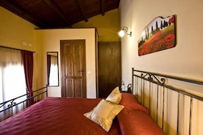 A bedroom with a large bed, a wooden door, a wall-mounted light fixture, and a painting. - Casale del Golfo (Alcamo)